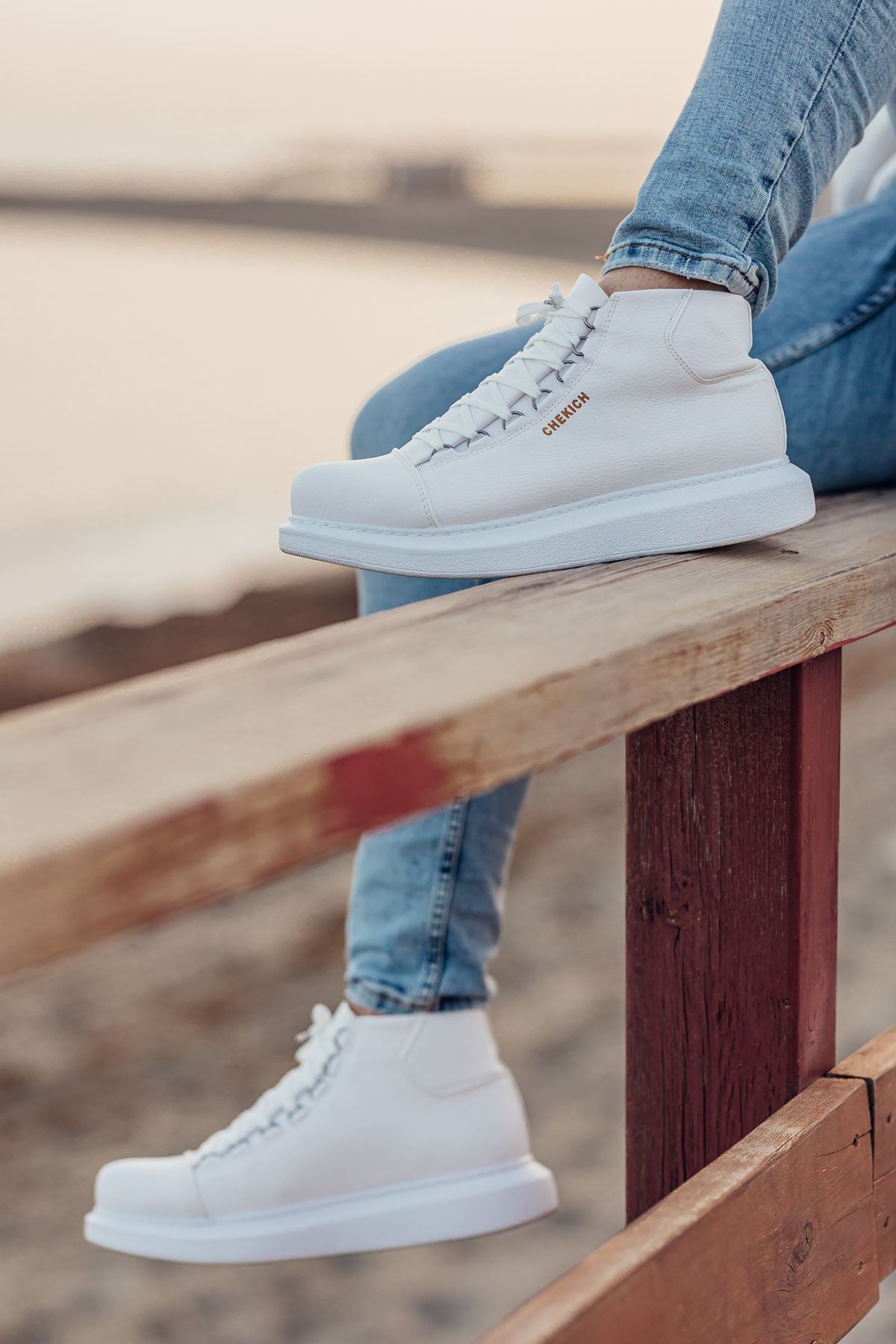 White lace-up boots shown on a wooden railing with denim cuffs