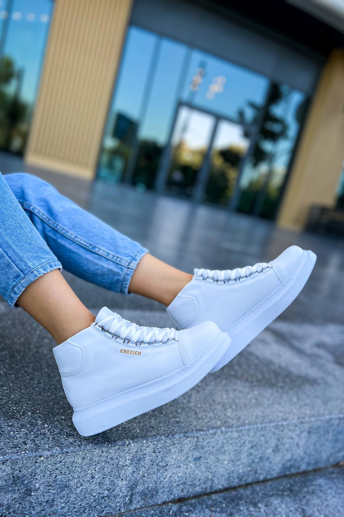 White lace-up boots with thick rubber sole, positioned on a concrete ledge