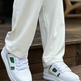 Men's white green low-top sneakers with thick sole, side view on wooden floor