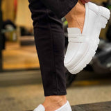 White slip-on loafers with strap detail and thick outsole, worn with dark pants