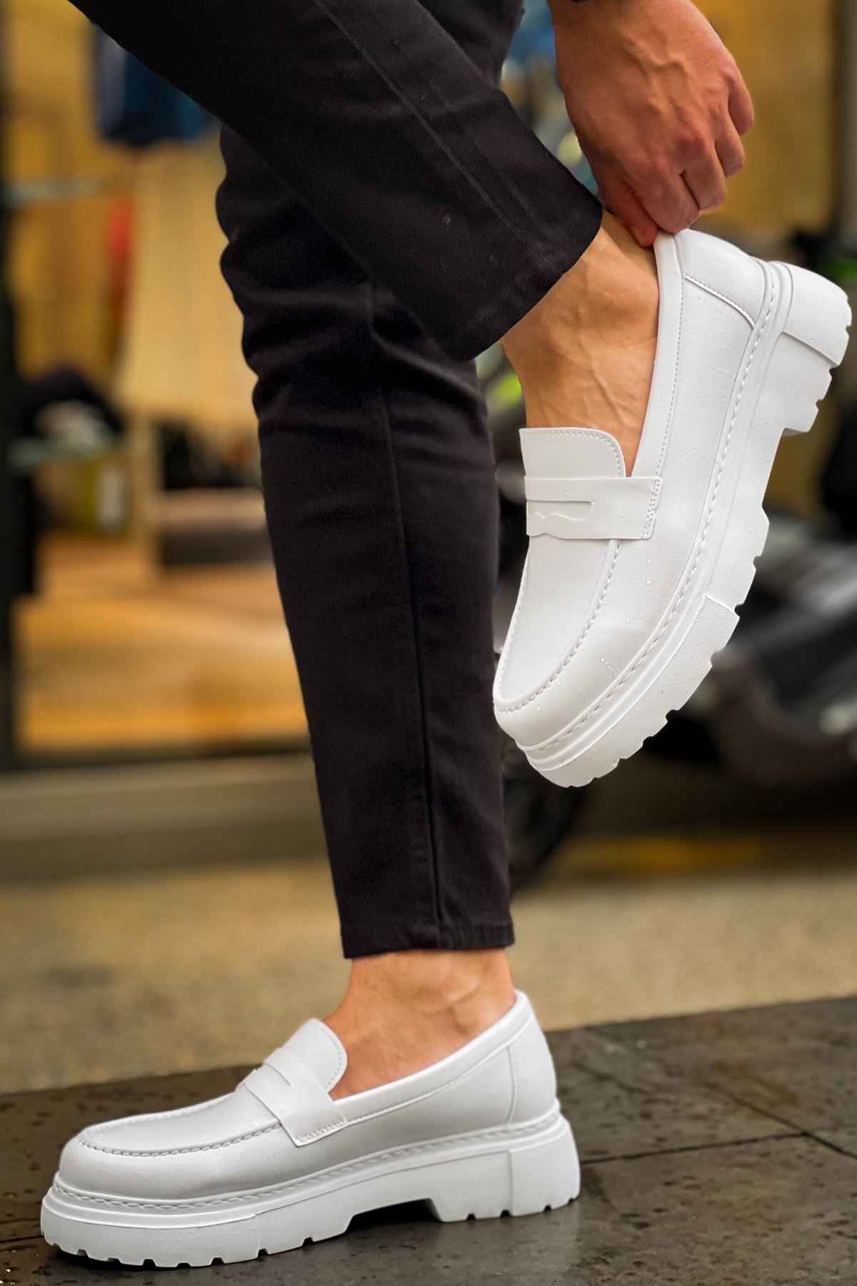 White slip-on loafers with strap detail and thick outsole, worn with dark pants