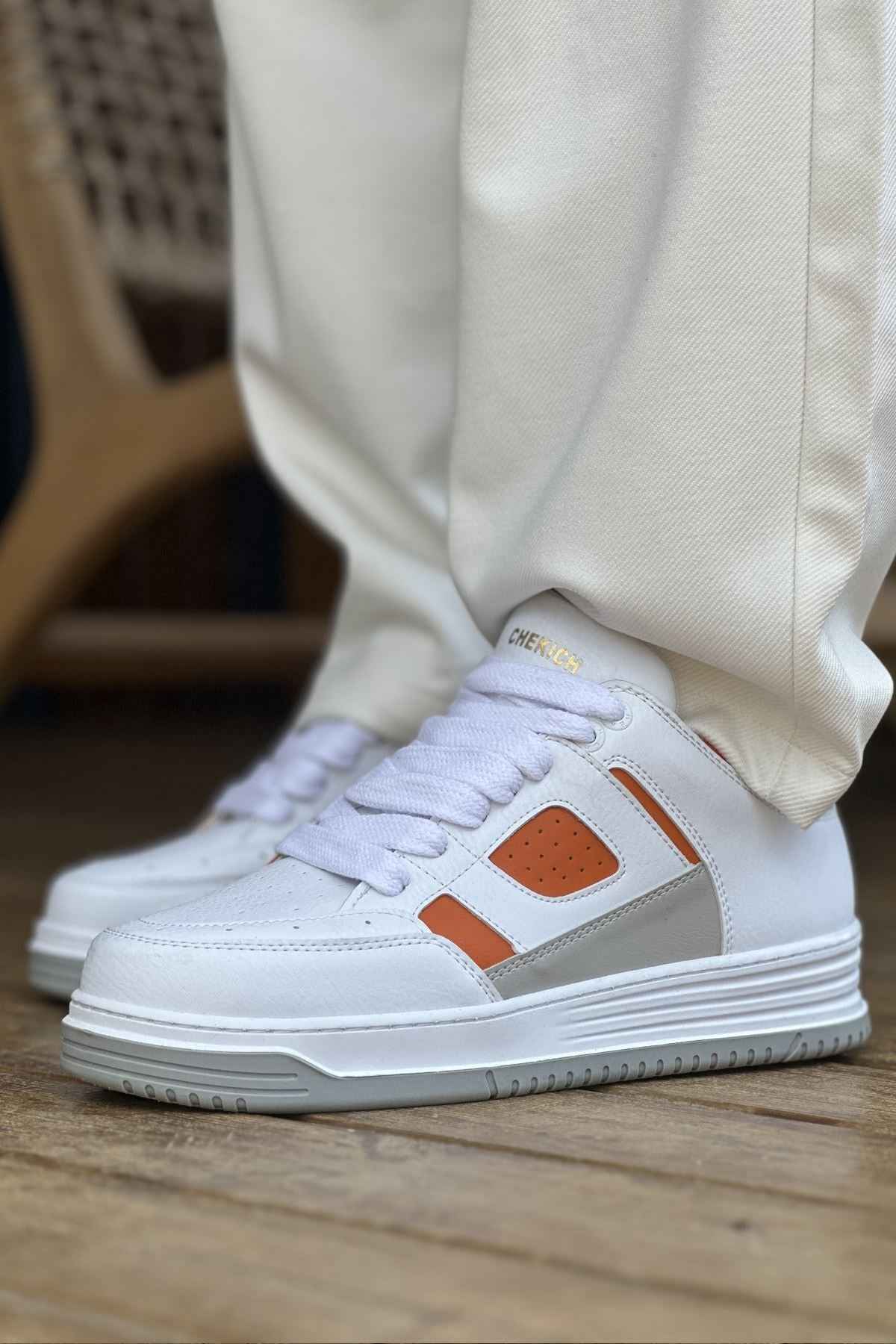 White lace-up sneakers with orange square logo on side and perforated toe