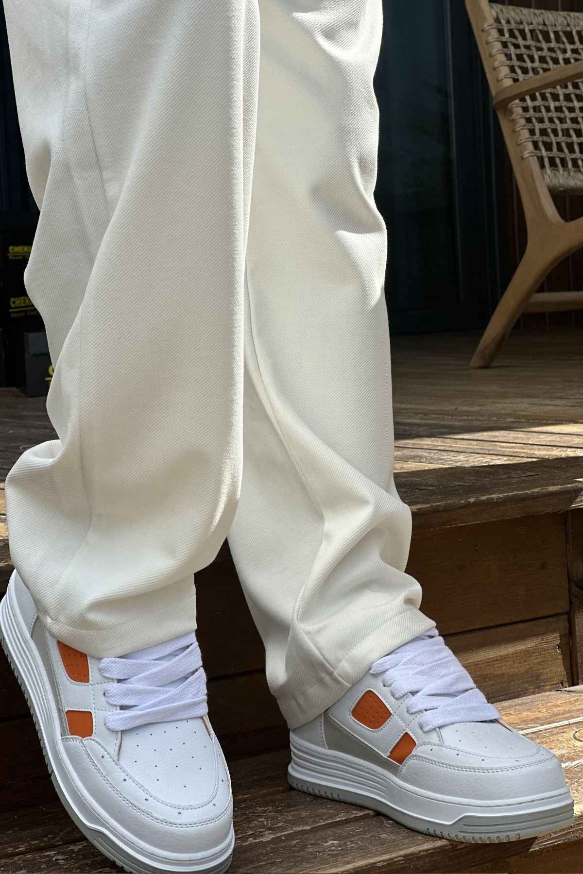 White sneakers with orange accents and thick gray sole, worn with white pants