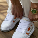 White lace-up sneakers with orange side squares and gray outsole, front close-up