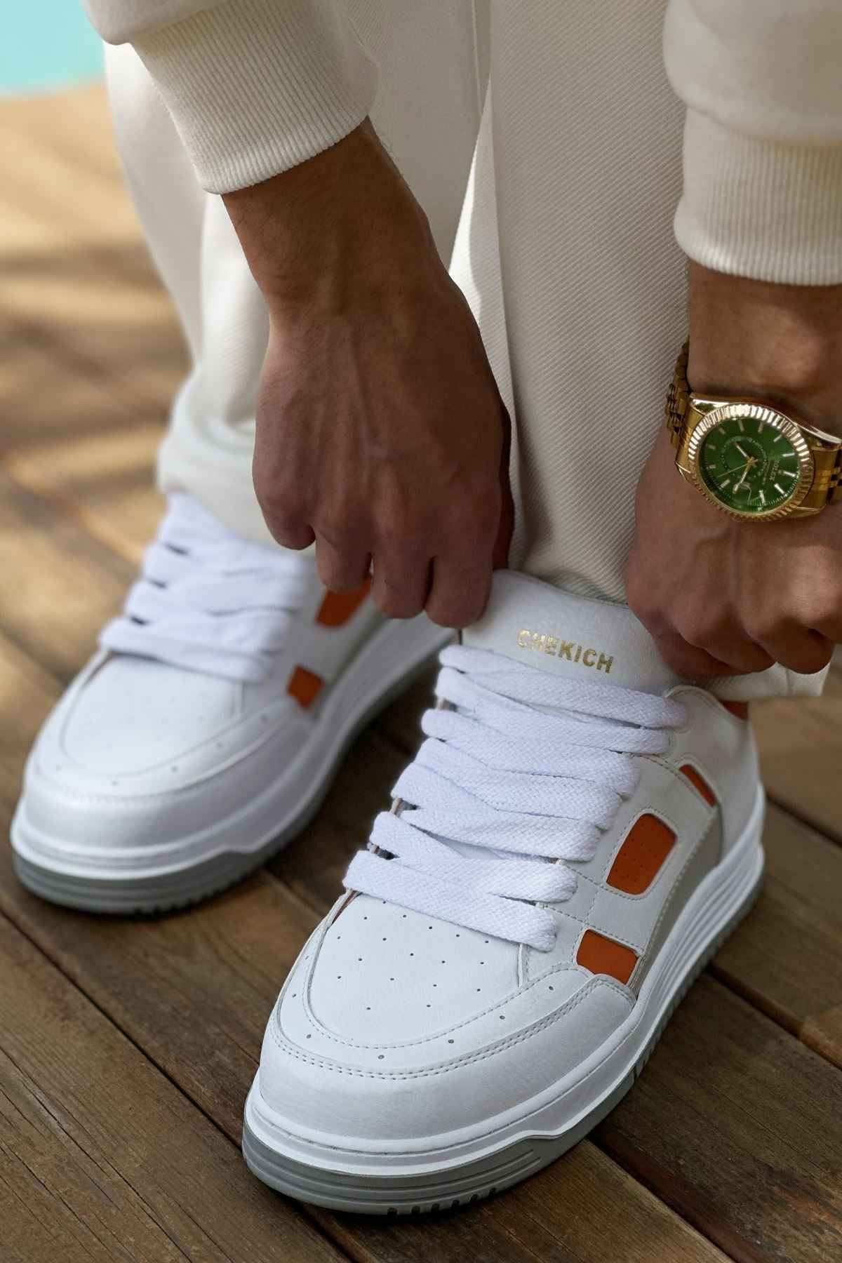 White lace-up sneakers with orange side squares and gray outsole, front close-up