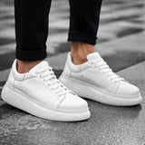 Pair of white low-top sneakers with laces and rubber soles under pants