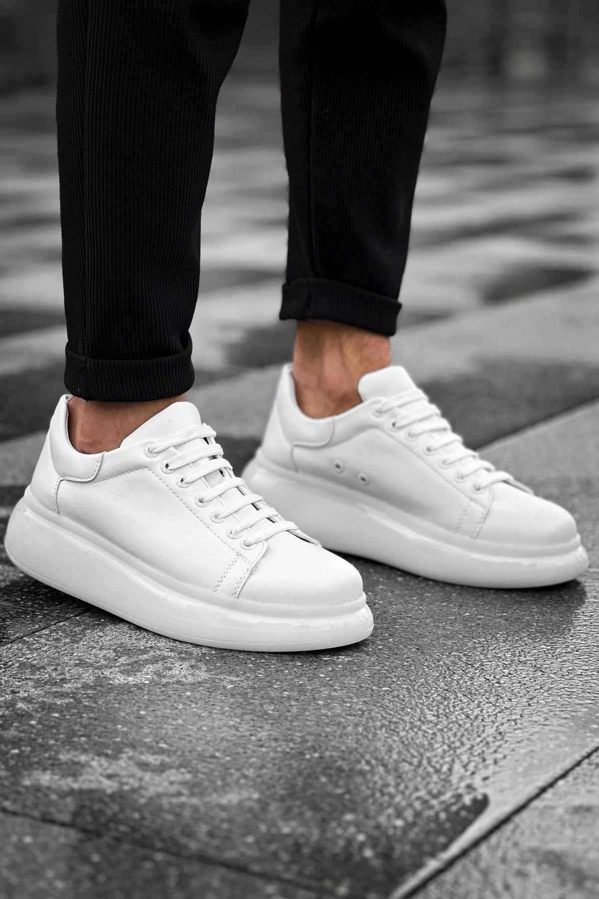 Pair of white low-top sneakers with laces and rubber soles under pants