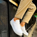 White low-top lace-up sneakers with side stitching detail, shown near a ledge