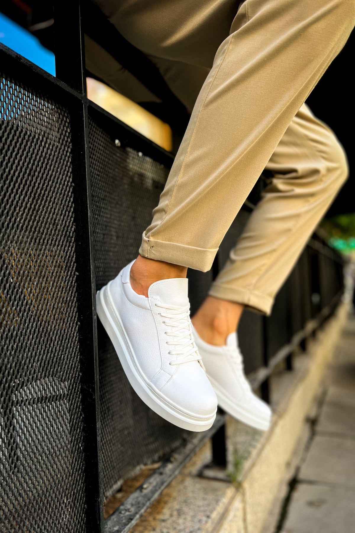 White low-top lace-up sneakers with side stitching detail, shown near a ledge